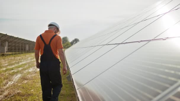 Professionell manlig ingenjör i skyddande hjälm promenad på ekologiska solkraftverk konstruktion. Begreppet elektricitet, ekologi, teknik. Solpanelernas gård. Produktion av ren energi. Grön energi — Stockvideo