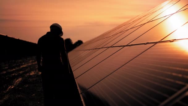 Asistenční technický pracovník v uniformě kontroluje provoz a účinnost fotovoltaických solárních panelů. Neznámý solární inženýr se dotýká solárních panelů rukou při západu slunce — Stock video
