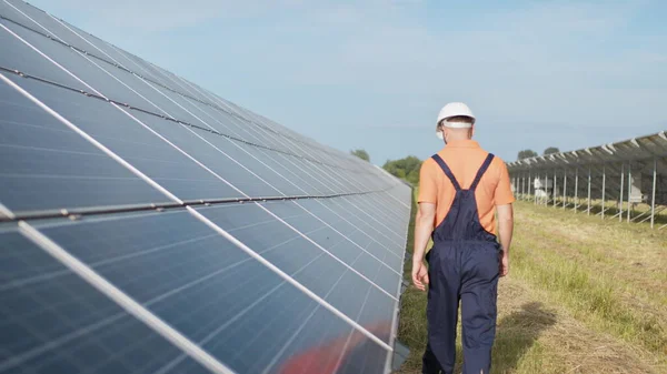 Mies teknikko kypärä kävelee uuden ekologisen aurinkorakenteen ulkona. Aurinkopaneelien tila. Aurinkosähköpaneelien toiminnan ja tehokkuuden tarkastus — kuvapankkivalokuva