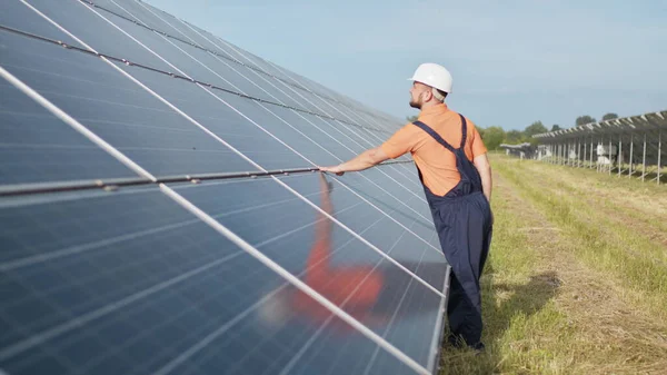 Nuori insinööri tarkistaa auringon toimintaa ja aurinkosähköpaneelien puhtautta. Uusiutuvan energian käsite. Käsitys aurinkovoimaloiden kehittämisestä ja vihreästä energiasta — kuvapankkivalokuva