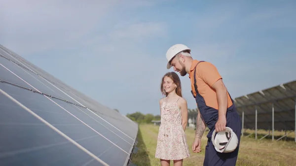 พ่อหนุ่มคนหนึ่งเป็นวิศวกรอธิบายให้ลูกสาวของเขาฟังถึงการดําเนินงานและประสิทธิภาพของแผงโซลาร์เซลล์แสงอาทิตย์ในตอนพระอาทิตย์ตก แนวคิด: พลังงานทดแทน, เทคโนโลยี, ไฟฟ้า, สีเขียว, อนาคต, ครอบครัว — ภาพถ่ายสต็อก