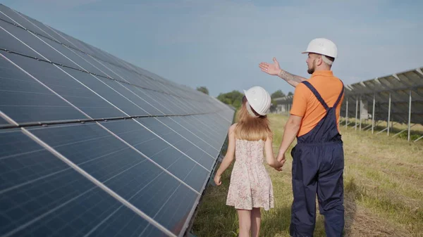 Aurinkovoimalassa työskentelevä isä kertoo tyttärelleen työstään, osoittaa vihreää energiaa, aurinkopaneeleita. Ampuminen aurinkovoimalassa. Maapallon suojelu, ilmaston lämpeneminen — kuvapankkivalokuva