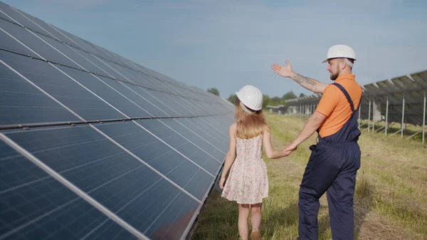 一位在太阳能发电厂工作的父亲告诉他的女儿他的工作，展示绿色能源，太阳能电池板。在一个太阳能发电厂拍摄。保护我们的地球，全球变暖 — 图库照片