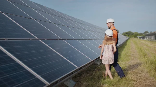 Aurinkovoimalassa työskentelevä isä kertoo tyttärelleen työstään, osoittaa vihreää energiaa, aurinkopaneeleita. Ampuminen aurinkovoimalassa. Maapallon suojelu, ilmaston lämpeneminen — kuvapankkivalokuva