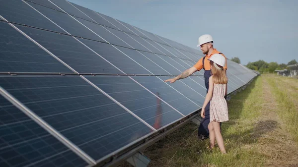 A father working in a solar power plant tells his daughter about his work, shows green energy, solar panels. Shooting at a solar power plant. Preservation of our planet, global warming