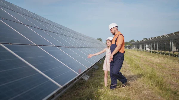 Um pai trabalhando em uma usina de energia solar conta a sua filha sobre seu trabalho, mostra energia verde, painéis solares. A disparar contra uma central solar. A criança estuda energia solar — Fotografia de Stock