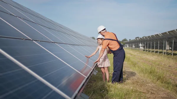 Aurinkovoimalassa työskentelevä isä kertoo tyttärelleen työstään, osoittaa vihreää energiaa, aurinkopaneeleita. Ampuminen aurinkovoimalassa. Lapsi tutkii aurinkoenergiaa — kuvapankkivalokuva