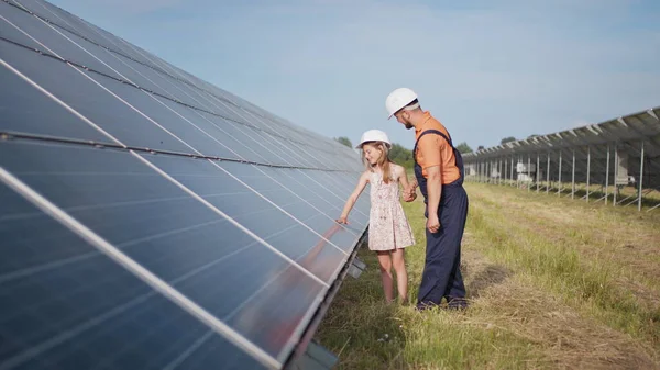 A father working in a solar power plant tells his daughter about his work, shows green energy, solar panels. Shooting at a solar power plant. The child studies solar energy