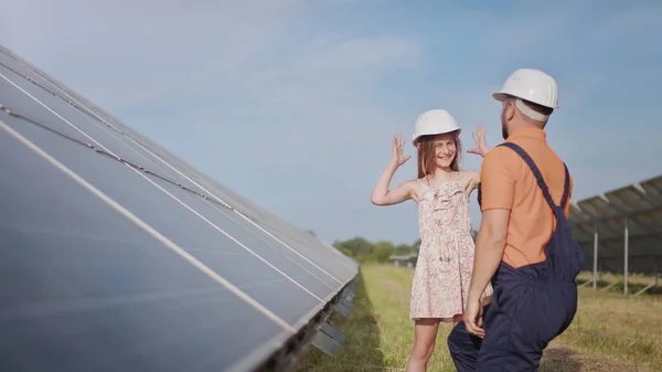 En ung far er ingeniør og forklarer sin lille datter en operasjon og oppvisning av solcellepaneler ved solnedgang. Konsept: Fornybar energi, teknologi, elektrisitet, grønn, framtid, familie – stockfoto