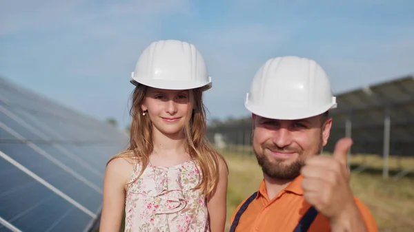 Father with little girl at solar power plant. The father talks about solar energy. The concept of green energy will save the planet for children. The father puts a protective helmet on the girls head