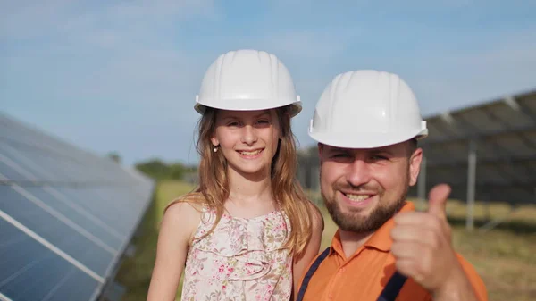 Isä ja pieni tyttö aurinkovoimalassa. Isä puhuu aurinkoenergiasta. Vihreän energian käsite säästää planeettaa lapsille. Isä laittaa tyttöjen päähän suojakypärän. — kuvapankkivalokuva