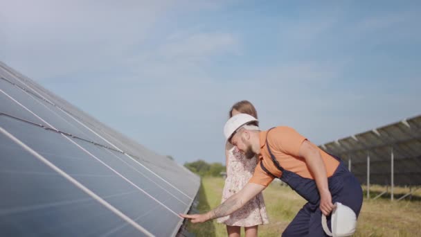 An young father is engineer explains to his little daughter an operation and performance of photovoltaic solar panels at sunset. Concept:renewable energy, technology, electricity,green,future, family — Stock Video