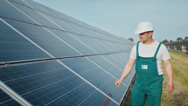 Engineer is checking the operation of sun and cleanliness of photovoltaic solar panels. Concept renewable energy. Caucasian man in hard helmet examining object solar panels. Concept of green energy — Stock Video