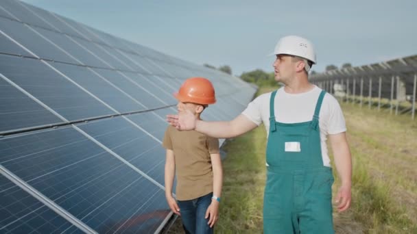 Engineer father is explaining to his little son an operation and performance of photovoltaic solar panels. Father and son happy Family concept. Boy and his dad engineer architect with safety helmets — Stock Video