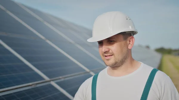 Portrett av en lykkelig mannlig ingeniør i beskyttelseshjelm foran kamera. Kjekk mann i uniform som smiler mens han står på solenergifarmen. Begrepet grønn energi. Økologisk framtid. – stockfoto