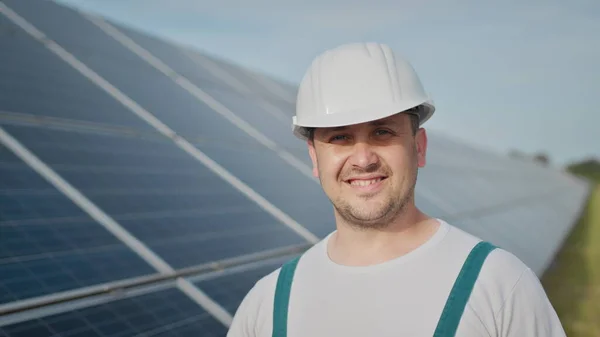 Portrett av en lykkelig mannlig ingeniør i beskyttelseshjelm foran kamera. Kjekk mann i uniform som smiler mens han står på solenergifarmen. Begrepet grønn energi. Økologisk framtid. – stockfoto