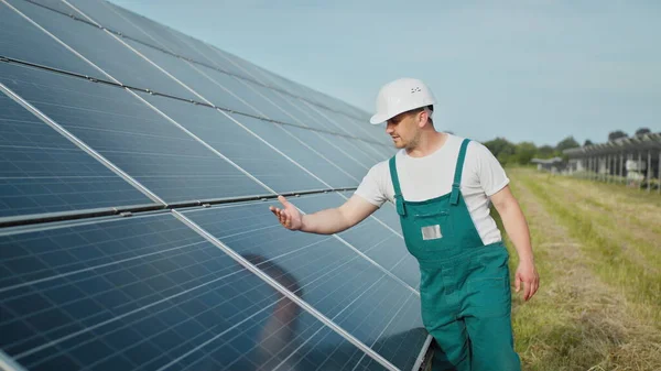 Insinööri tarkistaa auringon toimintaa ja aurinkopaneelien puhtautta. Uusiutuvan energian käsite. Valkoihoinen mies kovassa kypärässä tutkii esinettä aurinkopaneelit. Vihreän energian käsite — kuvapankkivalokuva