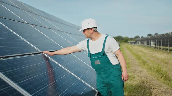 공학자는 태양의 작용 과 광전 지판의 청결 상태를 조사하고 있다. 재생 가능 에너지의 개념. 단단 한 헬멧을 쓰고 태양 전 지판을 검사하는 백인이야. 녹색 에너지 의 개념 — 스톡 사진