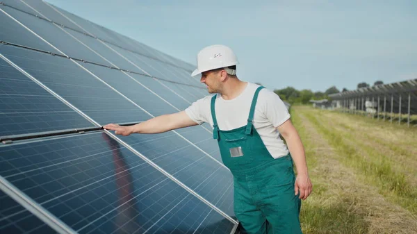 Insinööri tarkistaa auringon toimintaa ja aurinkopaneelien puhtautta. Uusiutuvan energian käsite. Valkoihoinen mies kovassa kypärässä tutkii esinettä aurinkopaneelit. Vihreän energian käsite — kuvapankkivalokuva