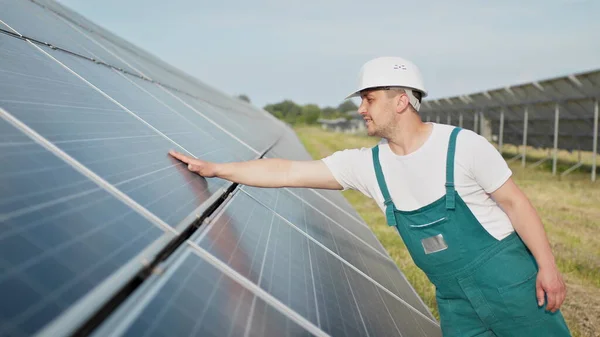 Porträt eines stolzen Arbeiters in Uniform, der mit großen Solarbatterien auf dem Feld steht. Ökologischer Bauernhof. Solarkraftwerk. Menschen. Nachhaltige Energie. Solarfeld. Ökologie. — Stockfoto