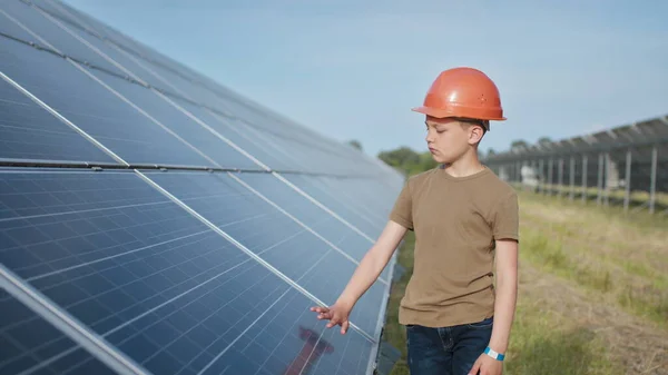 태양 전 지판 근처에 있는 아이의 초상화. 보호용 헬멧을 쓴 한 소년 이손으로 태양 전 지판을 건넌다. 태양열 발전소에서 촬영. 생태 농장. 태양열 발전소. 사람들 — 스톡 사진