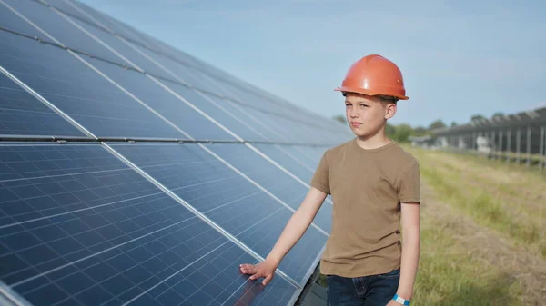 Portrait d'un enfant près des panneaux solaires. Un petit garçon avec un casque de protection touche les panneaux solaires avec sa main. Tir sur une centrale solaire. Ferme écologique. Centrale solaire. Les gens — Photo