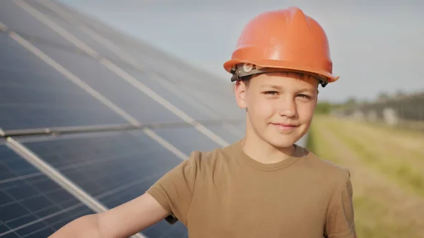 En liten gutt i beskyttelseshjelm på et solkraftverk. Begrepet barn og grønn energi. Barn for ren energi. Skyting på et solkraftverk. Økologisk gård. Solkraftverk – stockfoto