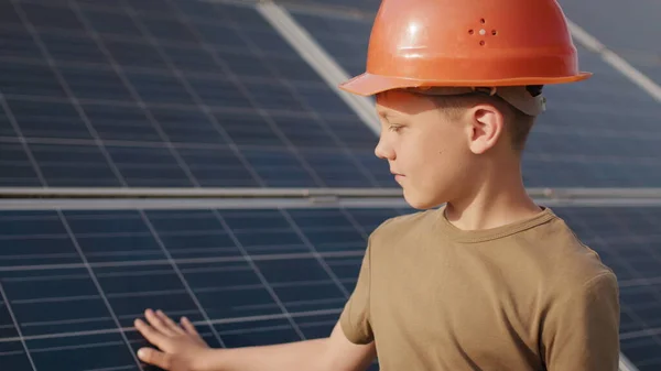 En liten gutt i beskyttelseshjelm på et solkraftverk. Begrepet barn og grønn energi. Barn for ren energi. Skyting på et solkraftverk. Økologisk gård. Solkraftverk – stockfoto