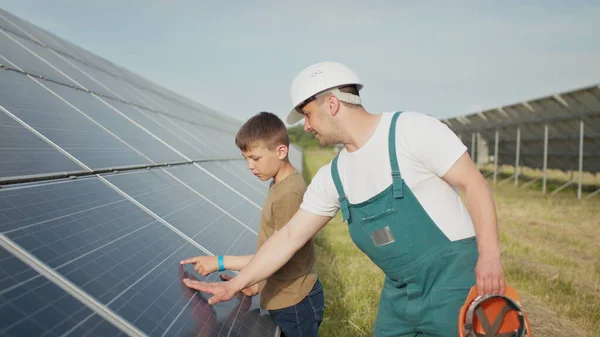 Молодий інженер-батько пояснює своєму маленькому синові операцію і продуктивність фотоелектричних сонячних панелей на заході сонця. Концепція: відновлювана енергетика, технології, електроенергія, зелене, майбутнє, сім'я . — стокове фото