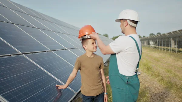 若いエンジニアの父親は、息子に日没時に太陽光パネルの操作とパフォーマンスを説明しています。概念:再生可能エネルギー、技術、電気、緑、未来、家族. — ストック写真