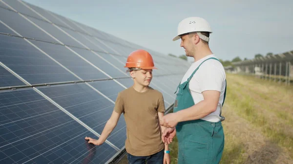 En ung ingeniørfar forklarer sin lille sønn en operasjon og forestilling av solcellepaneler ved solnedgang. Konsept: Fornybar energi, teknologi, elektrisitet, grønn, framtid, familie. – stockfoto