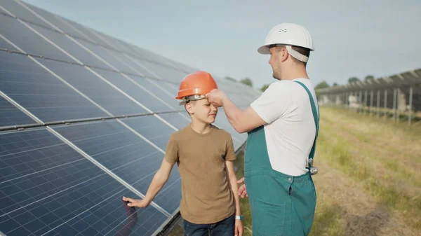 En ung ingeniørfar forklarer sin lille sønn en operasjon og forestilling av solcellepaneler ved solnedgang. Konsept: Fornybar energi, teknologi, elektrisitet, grønn, framtid, familie. – stockfoto