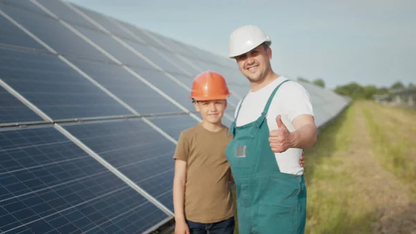 Um jovem pai engenheiro está explicando ao seu filho uma operação e desempenho de painéis solares fotovoltaicos ao pôr-do-sol. Conceito: energia renovável, tecnologia, eletricidade, verde, futuro, família. — Fotografia de Stock