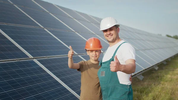 Um jovem pai engenheiro está explicando ao seu filho uma operação e desempenho de painéis solares fotovoltaicos ao pôr-do-sol. Conceito: energia renovável, tecnologia, eletricidade, verde, futuro, família. — Fotografia de Stock