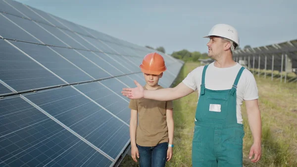 Ingeniørfar forklarer sin lille sønn en operasjon og forestilling av solcellepaneler. Far og sønn lykkelig familieopplegg. Gutt og hans far ingeniør arkitekt med vernehjelmer – stockfoto