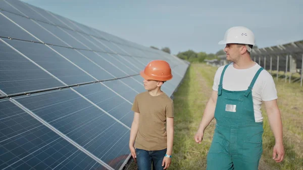 Ingeniørfar forklarer sin lille sønn en operasjon og forestilling av solcellepaneler. Far og sønn lykkelig familieopplegg. Gutt og hans far ingeniør arkitekt med vernehjelmer – stockfoto