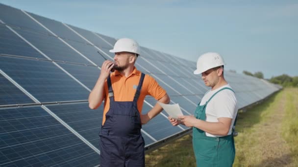 Técnico de energia verificando os painéis de células solares na energia da fazenda solar. Energia solar do inversor solar à eletricidade da fábrica. Um funcionário de uma usina transmite comandos por walkie-talkie. — Vídeo de Stock