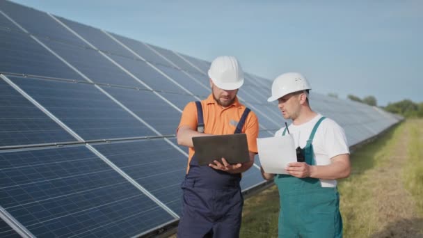 태양 전 지판 건설의 효율성을 확인하기 위해 디지털 태블릿을 읽는 정보를 사용하는 에너지 전문가. 녹색 에너지 직업. 기술. 두 명의 태양 발전소 근로자들 이 자료를 기록하고 있다 — 비디오