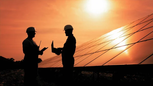 Kaksi tunnistamatonta aurinkoenergiainsinööriä taustavalossa auringonlaskun aikaan. Työtovereiden ryhmä, joka seuraa aurinkosähköpaneeleita auringonlaskun aikaan. Aurinkopaneeli Vaihtoehtoisen energian käsite — kuvapankkivalokuva