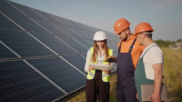 Trzech pracowników elektrowni alternatywnych spacerujących i mówiących o schemacie paneli słonecznych. Praca zespołowa. Grupa specjalistów. Kamera śledzi ludzi. Spotkanie z inwestorem — Zdjęcie stockowe