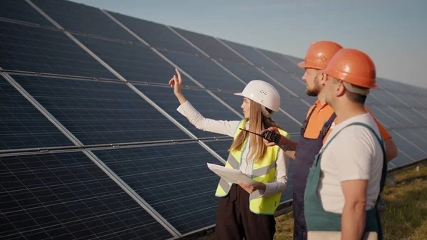 Três funcionários de usina de energia alternativa andando e falando sobre o esquema de painéis solares. Trabalho em equipa. Grupo de especialistas. A câmara segue as pessoas. Encontro com o investidor — Fotografia de Stock