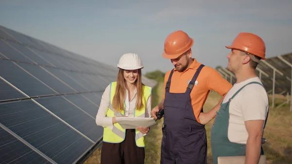 Insinöörit käyttävät piirustuksia aurinkopaneelilla erityisessä tasaisessa seisovassa katseessa keskustelemaan aurinkoisten akkujen asennuksesta. Menestyksekäs yritys. Ekologinen rakenne. Aurinkopaneelit. Tiimityö — kuvapankkivalokuva