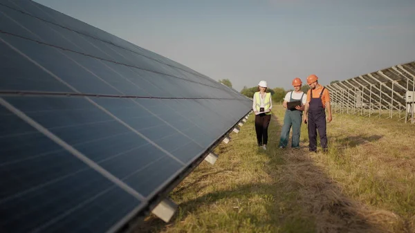 Teollisuusinsinöörien liiketiimi kävelee aurinkotilalla ja keskustelee tehokkaasta rakennussuunnitelmasta. Ekologinen asema. Vaihtoehtoista energiaa. Insinöörit käyttävät piirustuksia aurinko maatilalla — kuvapankkivalokuva