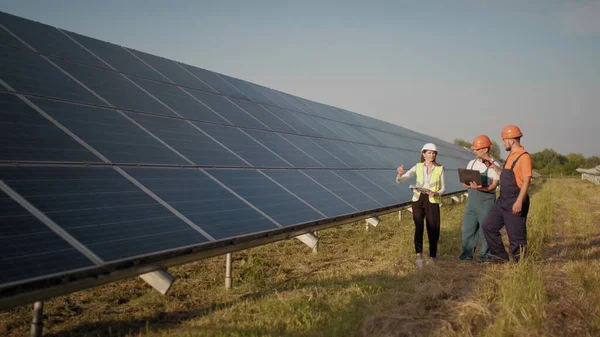 Industriingeniører som går på solfarmen og diskuterer en effektiv byggeplan. Økologisk stasjon. Alternativ energi. Ingeniører bruker tegninger på solparken – stockfoto