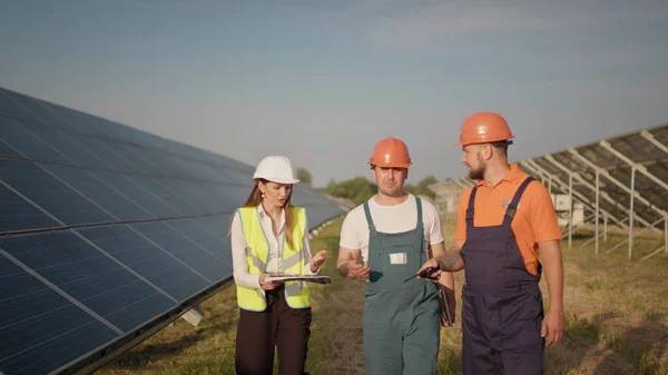 Monipuolinen insinöörit mies ja nainen tarkastaa aurinkopaneelit aurinkosähkövoimalaitoksen ulkona. Pari työntekijää, jotka tekevät yhteistyötä hallitakseen selkeää energiantuotantoa. Aurinkopaneelit. Ekologinen — kuvapankkivalokuva