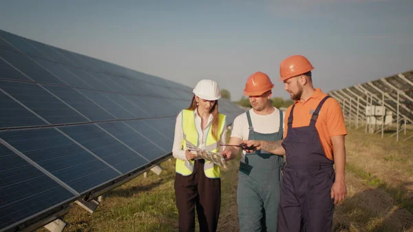 Monipuolinen insinöörit mies ja nainen tarkastaa aurinkopaneelit aurinkosähkövoimalaitoksen ulkona. Pari työntekijää, jotka tekevät yhteistyötä hallitakseen selkeää energiantuotantoa. Aurinkopaneelit. Ekologinen — kuvapankkivalokuva