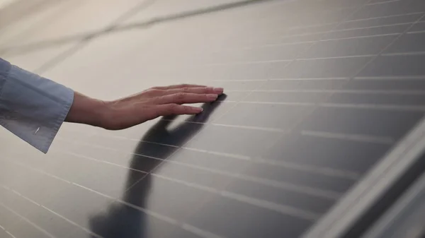 Eine Frau hält seine Hand über die Oberfläche der Sonnenblenden. Nahaufnahme eines jungen Ingenieurs Hand überprüft den Betrieb der Sonne und Sauberkeit von Photovoltaik-Sonnenkollektoren auf einem Sonnenuntergang. — Stockfoto