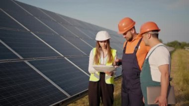 Alternatif enerji santralinin üç çalışanı yürüyor ve güneş panelleri hakkında konuşuyor. Takım çalışması. Bir grup uzman. Kamera insanları takip ediyor. Yatırımcıyla görüşme