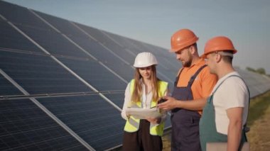 Mühendisler güneş çiftliğinde özel üniformalı çizimler yapıyorlar. Etrafa bakıyorlar ve güneşli bataryaların kurulumunu tartışıyorlar. Başarılı bir iş. Ekolojik yapı. Güneş panelleri alanı. Takım çalışması.