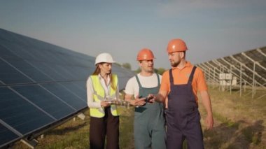 Çeşitli mühendis ve kadınlar dışarıdaki fotovoltaik elektrik santralindeki güneş panellerini inceliyor. Temiz enerji üretimini kontrol eden birkaç işçi. Güneş panelleri alanı. Ekolojik